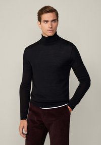 Maglione a collo alto nero dal design aderente, realizzato in tessuto morbido con maniche lunghe. Abbinato a pantaloni bordeaux scuri.