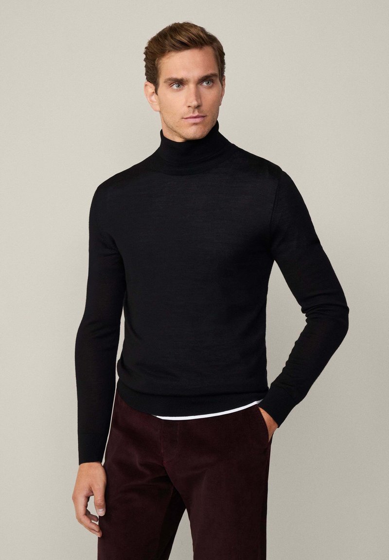 Maglione a collo alto nero dal design aderente, realizzato in tessuto morbido con maniche lunghe. Abbinato a pantaloni bordeaux scuri.
