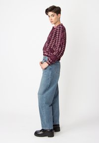 Sweat-shirt bordeaux à motifs avec des designs floraux, associé à un jean baggy bleu clair et des chaussures à plateforme noires. Coupe ajustée avec des manches longues.