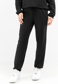 Black sweatpants made of soft fabric with a straight leg design and elastic waistband, paired with white sneakers.