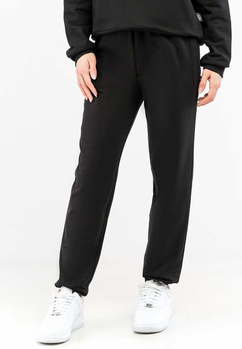 Black sweatpants made of soft fabric with a straight leg design and elastic waistband, paired with white sneakers.
