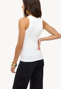 Wit geribbeld tanktop met hoge hals, gecombineerd met zwarte jeans. De outfit heeft een aangesloten ontwerp en minimale details.
