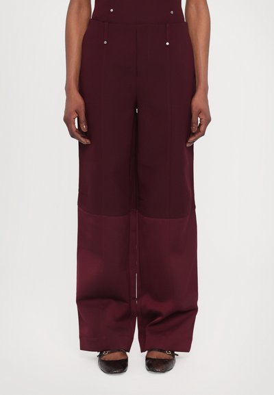 Pantalon large bourgogne en tissu lisse, doté d'une taille haute, de deux poches avant et d'accents en bouton argenté à la taille.