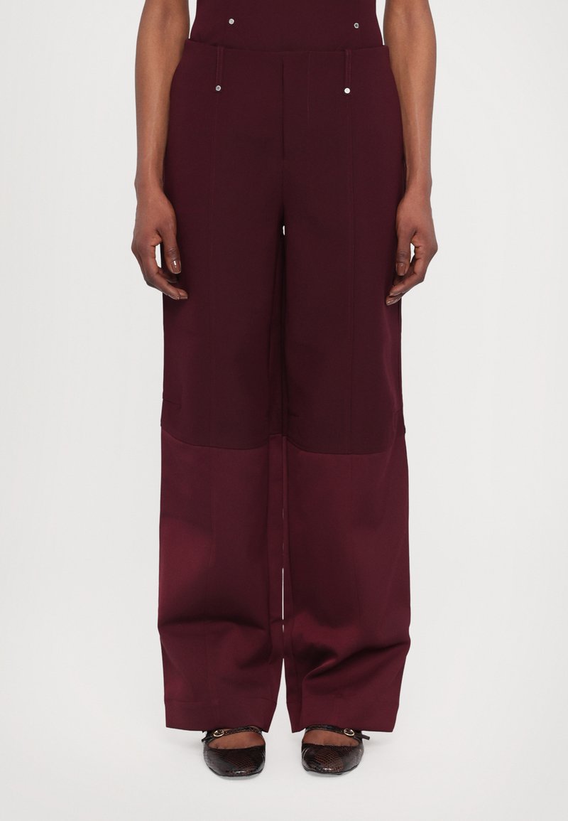 Pantalon large bourgogne en tissu lisse, doté d'une taille haute, de deux poches avant et d'accents en bouton argenté à la taille.