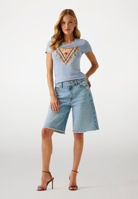 Gaiši zils īsās piedurknes T-krekls ar daudzkrāsainu trīsstūra grafiku un ziedu dekoriem, apvienots ar gaišiem džinsu bermudu šortiem.
