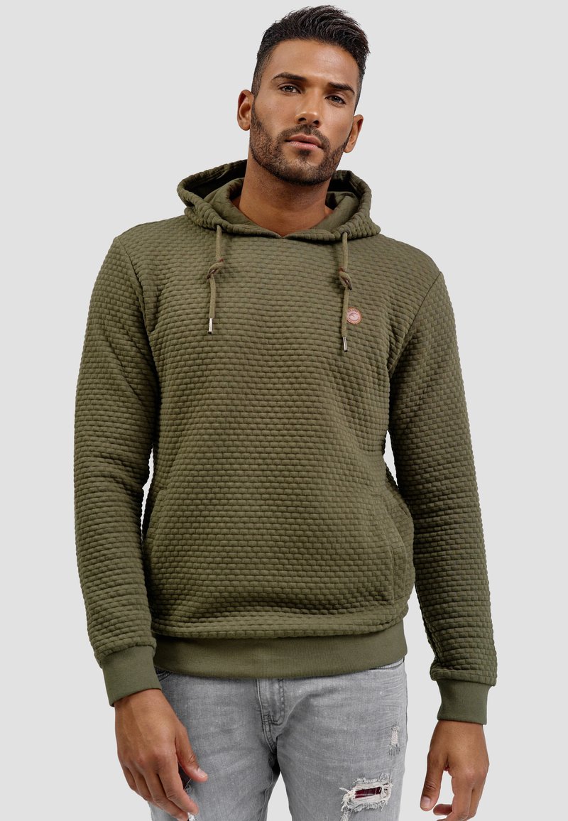 Sudadera color verde oliva con un patrón texturizado y acolchado, cordones ajustables y un parche redondo en el pecho; puños y dobladillo acanalados.