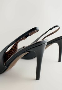 Zwarte leren slingback-hakken met een slanke stilettohak. Binnenkant met een luipaardprint patroon. Open teen ontwerp met uitgesneden zijkanten.
