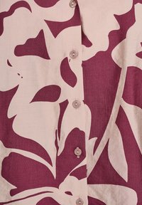 Camicia a bottoni con motivo floreale in un profondo bordeaux su uno sfondo beige chiaro. Presenta bottoni rosa pallido. Tessuto testurizzato.
