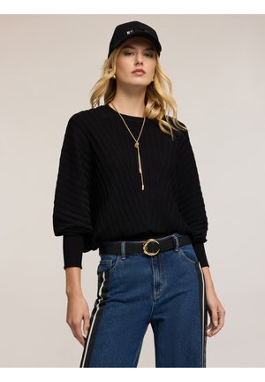 Maglione nero a coste con maniche lunghe, abbinato a jeans blu a vita alta con strisce verticali laterali e un berretto nero. Accento con collana d'oro.