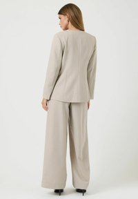 Lys beige skræddersyet jakkesæt med lange ærmer, lige benede bukser og en tætsiddende blazer. Glat tekstur med rene linjer og minimale detaljer.