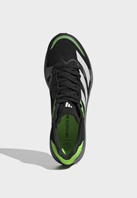 Scarpa atletica nera con accenti verdi e design a strisce bianche. Materiale superiore traspirante, punta rotonda e suola piatta in gomma.