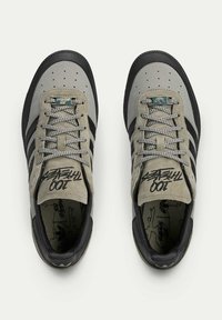 Gray and black sneakers with a textured fabric upper, black rubber sole, and three black stripes on the sides. Features lace-up design with branding.