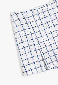 Geweven stof in het wit met een blauw ruitpatroon. De textuur lijkt iets verheven. De randen zijn netjes afgewerkt met een subtiele glans.