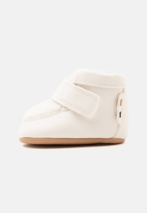 Chaussure bébé blanche souple avec une semelle beige et une large bande Velcro sur le dessus pour la fermeture et un port facile.