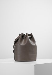 Ruskea nahkainen ämpärilaukku, jossa on pyöreä muoto, nyörikiristys ja sileä pinta. Mukana tasapohja, joka takaa vakauden.