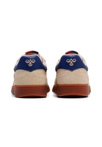 Sneaker in camoscio beige con accenti blu, suola in gomma marrone e emblema di un'ape sul tallone. Presenta un colletto imbottito e un tab di lacci rosso.