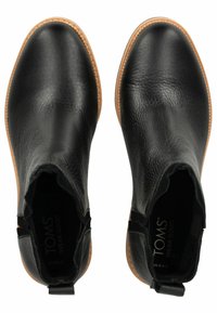 Bottines noires en cuir avec une finition texturée, des panneaux latéraux élastiques et une semelle en caoutchouc beige. Présentent la marque TOMS à l'intérieur.