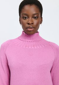 Rosa gestrickter Pullover mit einem gerippten hohen Kragen, der eine weiche Textur und lange Ärmel hat, ideal für lässige Anlässe.