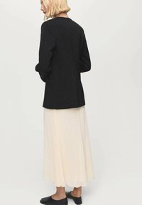 Blazer nero con maniche lunghe, abbinato a una gonna fluida color crema. L'outfit presenta un design semplice e si estende fino alla caviglia.