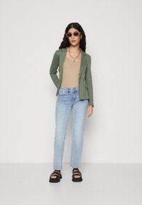 Blazer verde, maiou bej, blugi deschiși la culoare, sandale negre; colier cu lanțuri argintii suprapuse, ochelari de soare dreptunghiulari, materiale texturate.