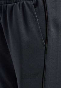 Svarta träningsbyxor med en slät yta, elastisk midja, sidoficka och diskret präglad logotyp nära fållen.