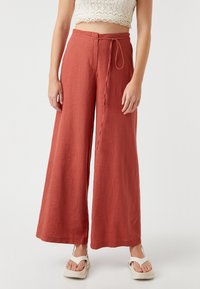 Pantalones de pernera ancha en color óxido, hechos de lino, con cintura ajustable y bolsillos laterales, con una textura suave y un corte relajado.