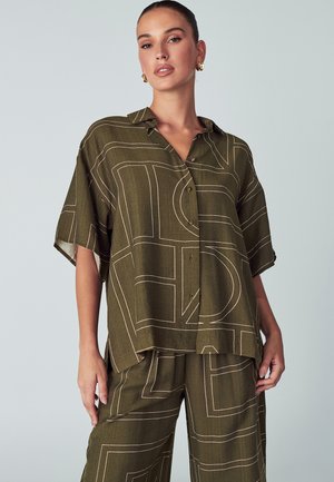 Olivgrünes Kurzarmhemd mit Kragen. Besteht aus einem geometrischen weißen Muster und hat eine Knopfleiste. Hergestellt aus einem strukturierten Stoff.