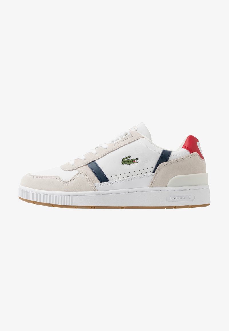 Baskets blanches avec des accents en daim beige et bleu marine, dotées de détails perforés, d'une semelle en caoutchouc et d'un capuchon de talon rouge. Logo Lacoste présent.