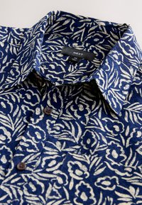 Tumesinise mustriga särk, millel on kreemikad lillemustrid. Kraega, nööpidega ja taskuga. Materjal on tekstuurse koega.