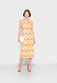 Vestido midi laranja com padrão floral branco, alças finas, silhueta ajustada e textura suave. Combinado com uma carteira branca e saltos laranjas.