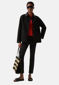 Černá bunda z vlněné směsi se šedým límcem, červený pletený top, černé kalhoty a pruhovaná černobéžová taška přes rameno. Černé nazouvací sandály.