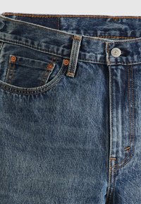 Denim jeans in medium blue wash with contrasting orange stitching. Features include a zipper fly, button closure, and five pockets.