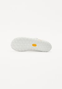 White rubber shoe sole featuring a zigzag tread pattern and yellow logo detail. The texture is smooth with raised gripping elements.