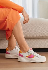 Sneakers bianchi con accenti rosa e arancione, pannello laterale testurizzato, chiusura con lacci davanti e dettaglio con zip sul retro, poggiati su una suola bianca spessa.
