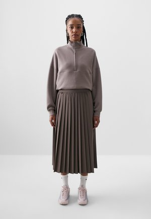 Grå zip-neck sweatshirt og en plissert midiskjørt, begge i en dempet taupefarge, kombinert med lyserøde sneakers og hvite sokker.