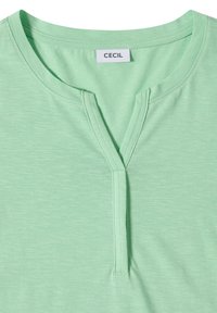 Chemise vert clair avec un col rond comportant une petite encoche en forme de V et une étiquette de marque "CECIL" visible à l'intérieur du col.
