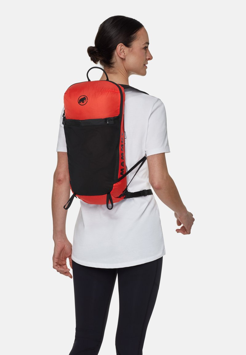 Zaino rosso e nero con spallacci regolabili, tessuto leggero, texture a griglia sulla parte superiore e un distintivo con logo al centro. Tasca frontale con zip.