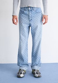 Lyseblå denimjeans med rutemønster, rett bendesign, fem lommer og knappeåpning. Brukt med svarte og gule sneakers.