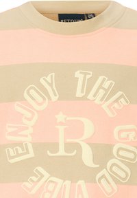 Jasnoróżowy i beżowy sweter w paski z wypukłymi białymi literami "CIESZ SIĘ DOBRYMI WIBRACJAMI" oraz stylizowanym akcentem "R" na środku.