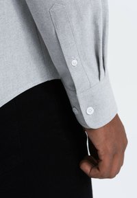 Vaaleanharmaa pitkähihainen paita, jossa on napilliset hihansuut, teksturoitu kangas ja slim fit -leikkaus, yhdistettynä tumman kankaan kanssa alla.