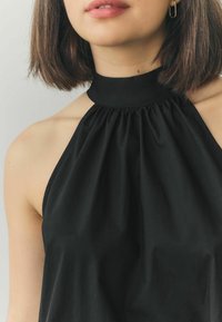 Svart halterneck-top med en samlad halsringning och slät yta. Har en figurnära krage och öppna axlar. Klassisk design.