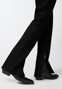 Pantalones negros acampanados con aberturas en el dobladillo, combinados con botas de cowboy de cuero negras con tacón bajo y textura suave.