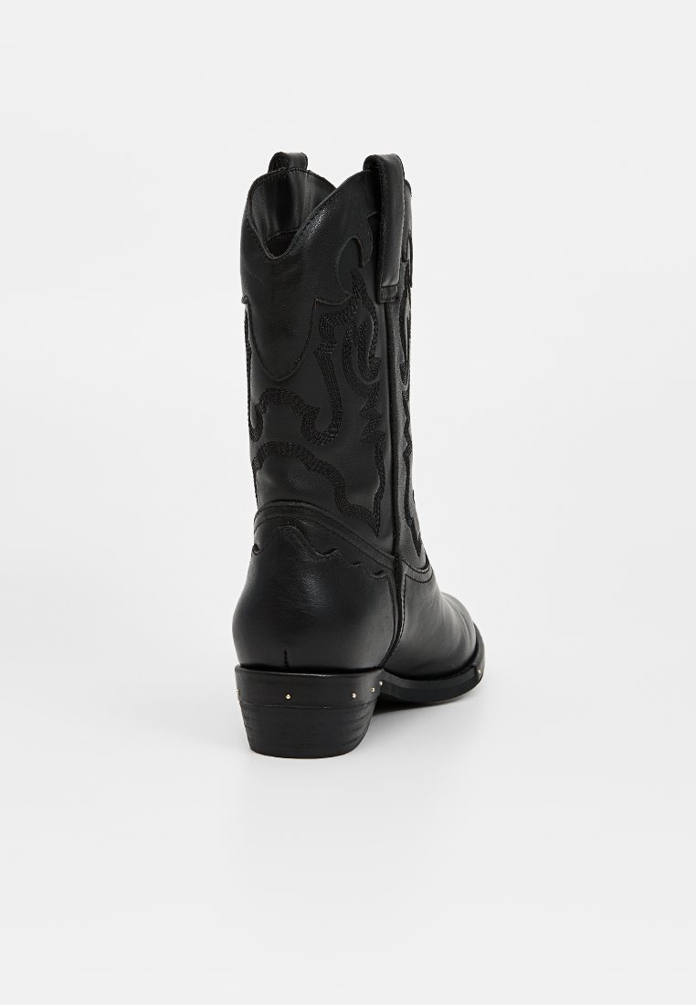 Bota de cowboy de cuero negro con acentos bordados, un tacón bajo y una parte superior curva. Textura lisa con detalles sutiles en los lados.