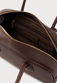 Smešasti smeđi ručni torbica s patentnim zatvaračem. Unutrašnjost sadrži džep s patentnim zatvaračem i oznaku. Zlatni patentni zatvarač i detalji šivanja su prisutni.