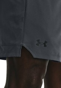 Pantalones cortos deportivos para hombre en gris oscuro con un acabado ligeramente texturizado, que cuentan con perforaciones transpirables y un logotipo negro cerca del dobladillo.