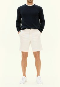 Marinblå tröja med rund halsringning, krämfärgade shorts och vita sneakers. Tyget verkar slätt, med en avslappnad passform, ren design och inga synliga mönster.