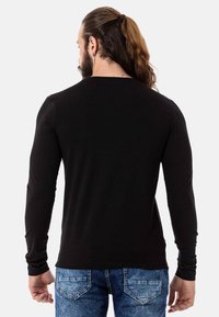 Schwarzes Langarmshirt mit figurbetonter Passform, aus weichem Material gefertigt. Getragen mit blauen Jeans im Denim-Look, was einen lässigen Stil zeigt.