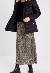 Svart puffjacka med foder i päls, dragkedjestängning och tryckknappar, tillsammans med en svart blommig maxikjol och svarta stövlar.