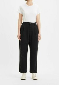 Pantaloni neri a vita alta con pince e tasche laterali, abbinati a una maglietta bianca a girocollo e sneaker color crema.