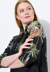 Schwarzes Kurzarmhemd mit botanischem Design aus Palmblättern und Giraffenmustern. Glattes Material mit lockerem Schnitt.